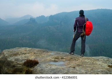 Hiker with red backpack on sharp sandstone rock in rock empires park and watching over the misty and foggy spring valley to Horizon.