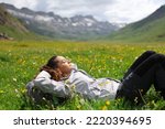 Hiker resting lying on the grass in a valley of a high mountain