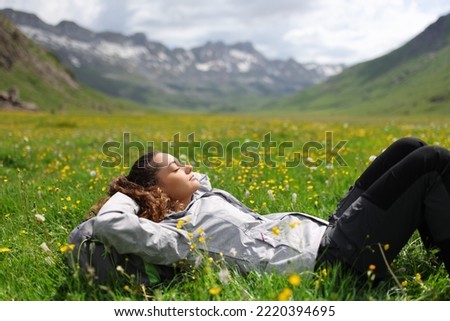 Hiker resting lying on the grass in a valley of a high mountain