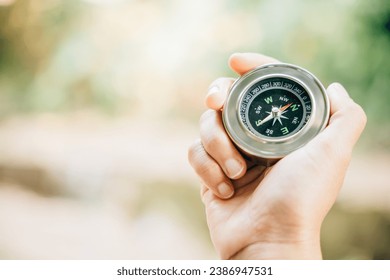 Hiker searches for direction in the forest holding a compass to overcome confusion. The compass in the hand signifies exploration and finding one way in the wilderness. - Powered by Shutterstock