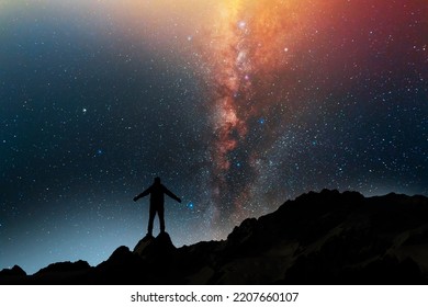 Hiker silhouette stands on the hill on and looks on the milky way galaxy. Dark starry night - Shutterstock ID 2207660107