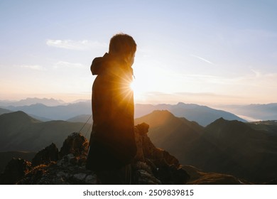 Hiker silhouetted against the rising sun on a mountain peak. - Powered by Shutterstock