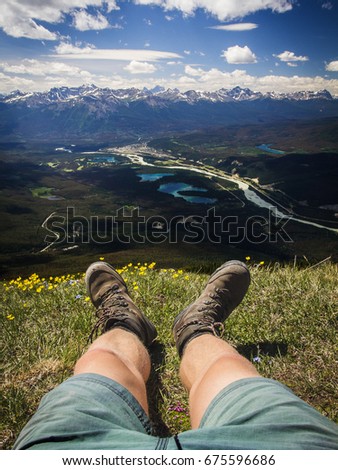Hiker sitting on the alpine meadow of Old Man Mountain in Jasper national park, Alberta, Canada. Hiking boots and muscled calf, town of Jasper, turquoise, cyan lakes, mountains in background. Sunny.