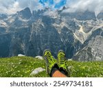 Hiker sitting on colorful meadow looking at cloud covered rugged mountain peak of majestic Brenta Dolomites, Trentino, Italy. Wanderlust in alpine wilderness. Hiking in pristine Italian Alps in summer