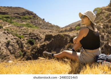 A hiker sitting on a rocky cliff, enjoying the scenic view of a mountain valley during a summer hiking adventure, embodying relaxation and the beauty of nature. - Powered by Shutterstock
