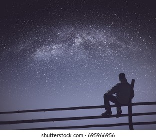 Hiker sitting on a wooden fence under the starry sky with milky way. Fairy night. Instagram stylization. - Powered by Shutterstock
