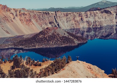 A hiker standing at an edge on Garfield Peak Trail at Crater Lake National Park, Oregon, USA.  Views of Wizard Island and lake reflections on a sunny calm day.  - Powered by Shutterstock