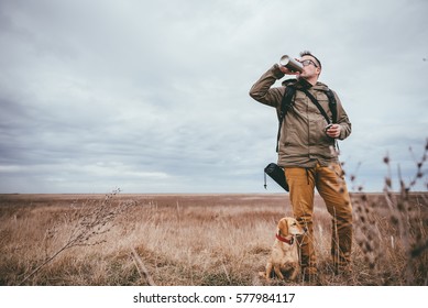 Hiker standing in grassland with a dog and drinking water - Powered by Shutterstock