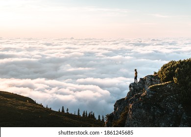 Hiker standing on cliff edge and looking at view on montain summit. Young climber enjoying sunrise or sunset looking at the cloud inversion. Travel, sport and active life concept in Ceahlau Massiff