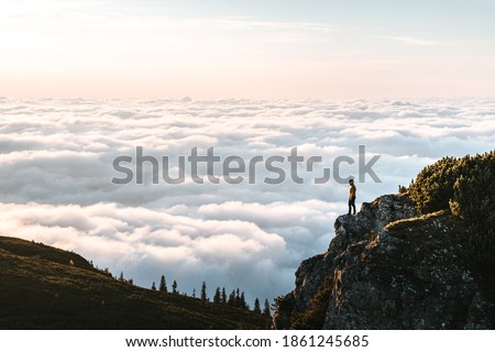 Hiker standing on cliff edge and looking at view on montain summit. Young climber enjoying sunrise or sunset looking at the cloud inversion. Travel, sport and active life concept in Ceahlau Massiff