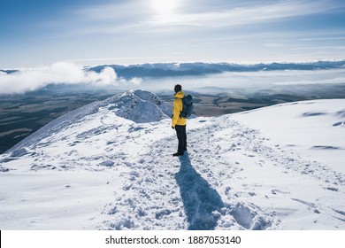 Hiker stands and enjoys valley view from hilly viewpoint. Hiker reached top of the mountain. Adventure ascent of alpine peak in snow
