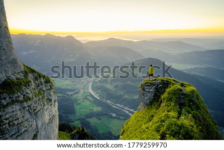 Hiker stands and enjoys valley view from hilly viewpoint. Traveling on hill peaks landscape. Sport, tourism and hiking concept. Watching sunset.