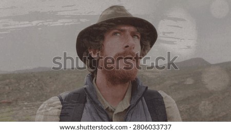 Hiker studying folded map, lifting head and scanning horizon, film-scratch overlay confirming route. Outdoorsman, explorer, backpacker, landscape, upland, overcast, filmgrain