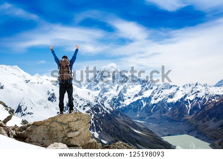 hiker at the top of a rock with his hands raised enjoy sunny day