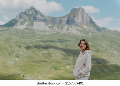 Hiker tourist girl standing on top of the mountain and enjoying valley view. Happy woman with her arms outstretched, freedom and happiness, achievement in mountains