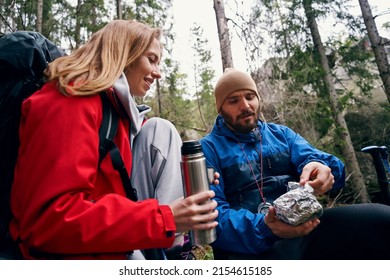 Hiker unpacking meal from tinfoil near woman in forest
