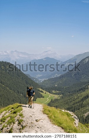 Hiker walking down steep alpine trail overlooking valley, French Alps