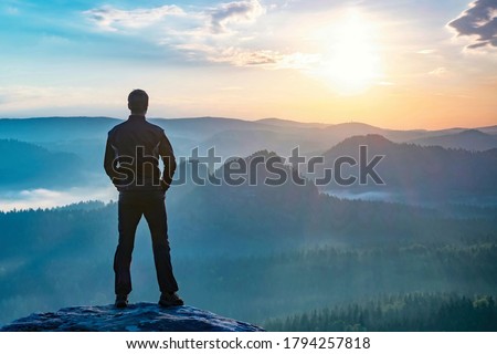 Hiker watching to autumn Sun at horizon . Beautiful moment. Spectacular mountain ranges silhouettes. Man reaching summit enjoying freedom