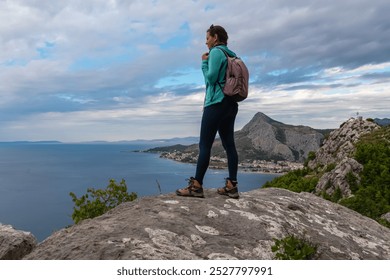 Hiker woman with backpack on rock formation with aerial scenic view of coastal town Omis in Dinara mountains, Split-Dalmatia, Croatia, Europe. Coastline of Adriatic Sea, Balkans. Travel destination - Powered by Shutterstock