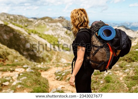 Hiker woman equipped with trekking backpack with sleeping bag and mat standing contemplating the landscape. Sport and outdoor adventure