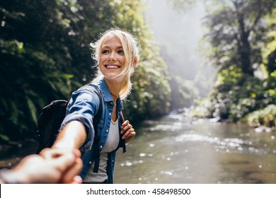 Hiker woman holding man's hand and leading him on nature outdoor. Couple in love. Point of view shot.