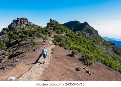 Hiker woman on scenic paved hiking trail winding up to mountain peak Pico Ruivo, Madeira island, Portugal, Europe. Path on rugged terrain of unique rock formations and deserted shrub land. Wanderlust - Powered by Shutterstock - Get 15% off with code: PIKWIZARD15