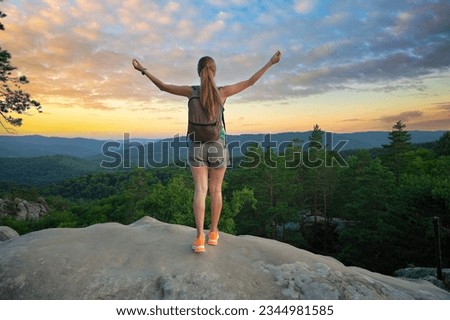 Hiker woman relaxing on mountain footpath raising up hands enjoying evening nature during travel on wilderness trail. Lonely female traveler traversing high hilltop route. Healthy lifestyle concept