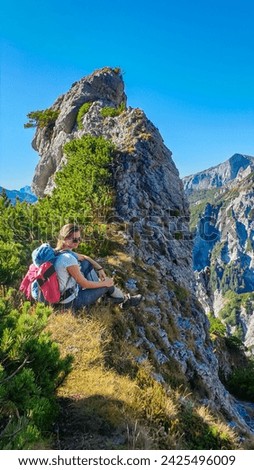 Hiker woman resting next to unique rock formation with panoramic view of majestic Hochschwab massif, Styria, Austria. Idyllic hiking trail in remote Austrian Alps. Sense of escapism, peace, reflection