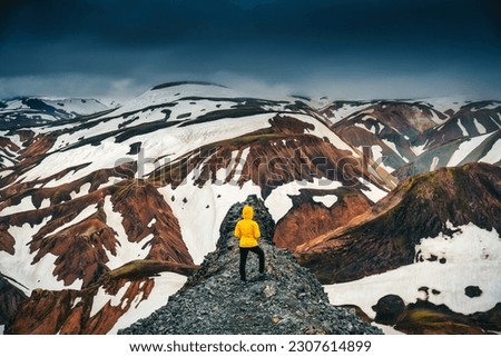 Hiker woman standing on peak of volcanic mountain with snow covered on Blanhjukur trail in summer at Landmannalaugar, Iceland
