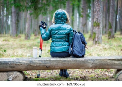 Hiker woman with trekking poles and backpack sitting on bench and relaxing