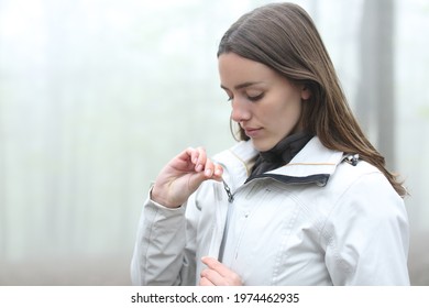 Hiker woman zipping the jacket ready to walk in a foggy forest - Shutterstock ID 1974462935