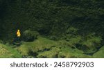 Hiker in yellow jacket in greenery. Background of moss-covered volcanic formations. Icelandic nature, wonders, exploring.