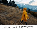 Hiker in Yellow Raincoat Walking on Trail in Woods with Mountain View and Travel Adventure Beauty in Nature Landscape Background