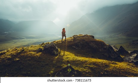 Hiker Young Woman With Backpack Rises To The Mountain Top Against Backdrop Of Sunset. Discovery Travel Destination Concept