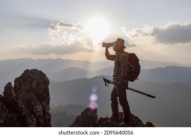 Hikers with backpacks holding binoculars looking on top of the rock mountain