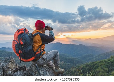 Hikers with backpacks holding binoculars sitting on top of the rock mountain