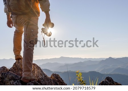 Hikers with backpacks holding binoculars standing on top of the rock mountain at sunset background