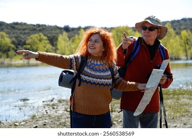 Hikers with backpacks and map pointing towards destination by lake, enjoying outdoor activity - Powered by Shutterstock