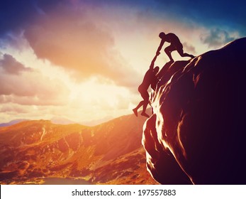 Hikers climbing on rock, mountain at sunset, one of them giving hand and helping to climb. Help, support, assistance in a dangerous situation - Shutterstock ID 197557883