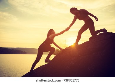 Hikers climbing on rock, mountain at sunset, one of them giving hand and helping to climb. Help, support, assistance in a dangerous situation