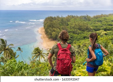 Hikers couple hiking on Kalalau trail overlooking beach coastal walk two tourists with backpacks walking outdoor in Kauai island, Hawaii summer travel leisure activity active lifestyle.