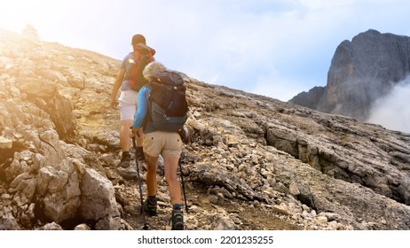 Hikers Couple Man And Woman Walk Backpack Rocks Mountains , Young Man And Elderly Woman Family Trek In Holiday Sun Summer .