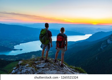 Hikers enjoying scenic view of valley with lake at sunset, couple enjoying summer outdoor trek in mountains, active lifestyle, two people
