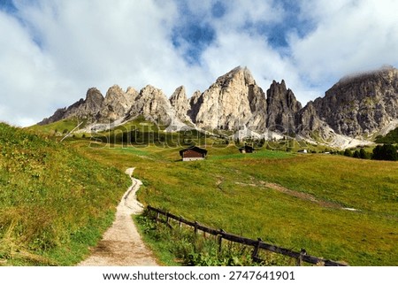 Hikers explore walking paths surrounded by mountains in Puez Odle Natural Park in Val Gardena Italy. Green fields and wooden structures are visible. Date: 01.09.2025 
