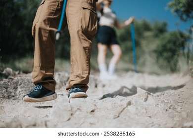 Hikers navigating a rocky trail on a sunny day, focusing on their hiking shoes and trekking poles for support and stability in the rugged terrain. - Powered by Shutterstock