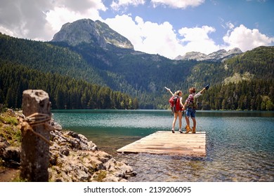 Hikers on wooden jetty by lake jumping in joy. Lifestyle, love, togetherness, nature concept