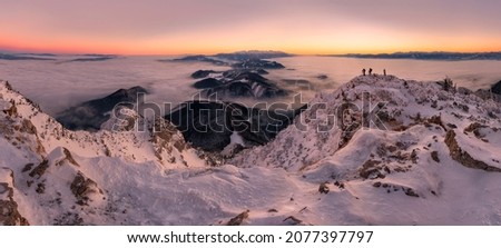 Hikers and photographers on top of a snowy hill before sunrise. View of the inversion in the mountain valleys. Mountains and hills in winter. Sunset panorama from peak Velky Choc, Slovakia 