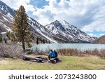 Hikers resting, sitting beside a isolated St Elias Lake in Kluane National Park during spring time, May with no other people. Snow capped mountains surrounding the scenic, Canadian view. 