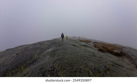 Hikers walking on a foggy mountain trail with rocky terrain. - Powered by Shutterstock