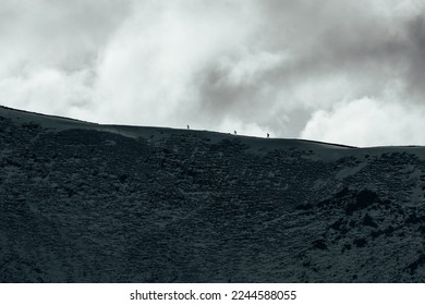 Hikers walking on a snow-covered ridge, silhoutted against a moody sky with grey clouds on a wintery day in the Lake District National Park in England.
